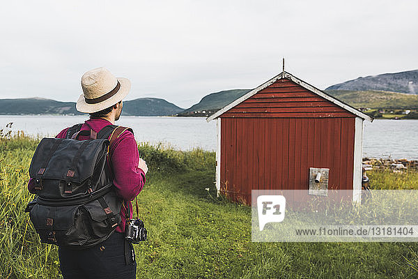 Junger Mann mit Rucksack erkundet rote Scheune in Nordnorwegen