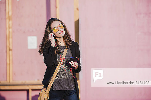 Junge Frau mit Handy und Kopfhörern mit farbiger Sonnenbrille