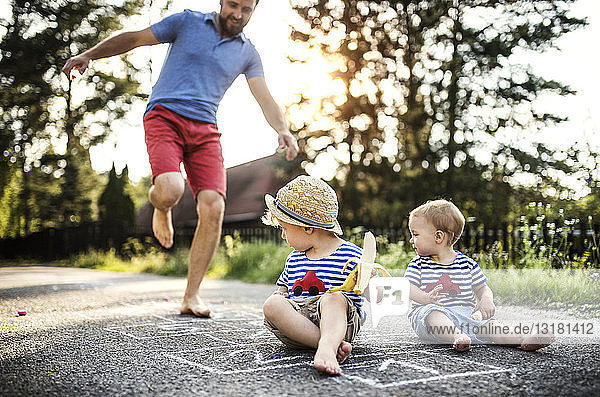 Mature man playing hopscotch while his little children watching him