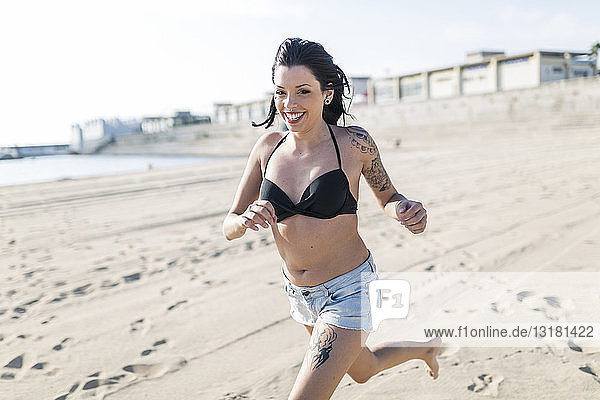 Porträt einer lächelnden jungen Frau mit Tätowierungen am Strand