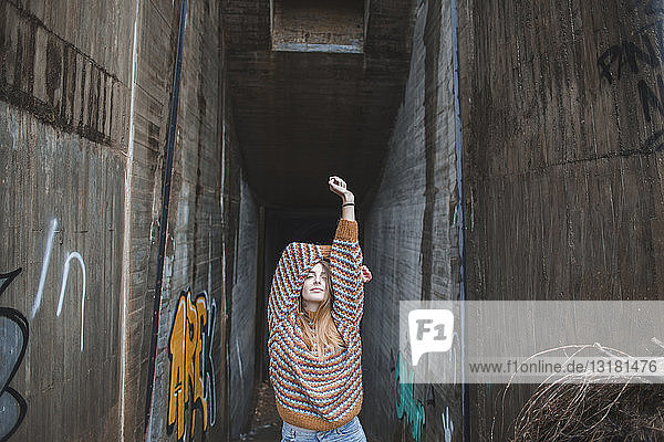 Porträt einer jungen Frau  die ihre Arme an einer Graffiti-Unterführung hebt