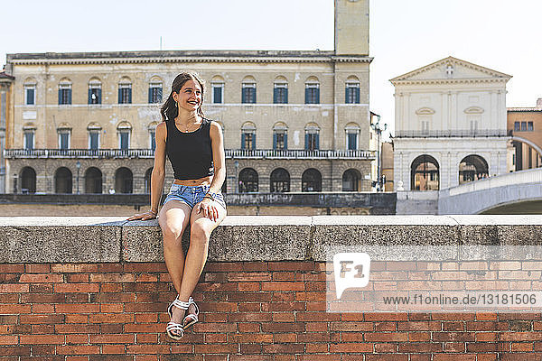 Italy  Pisa  young woman sitting on a wall in the city