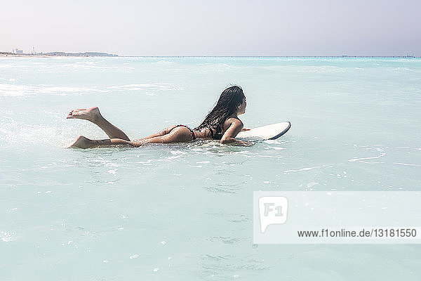 Junge Frau liegt auf einem Surfbrett  schwimmt auf dem Meer