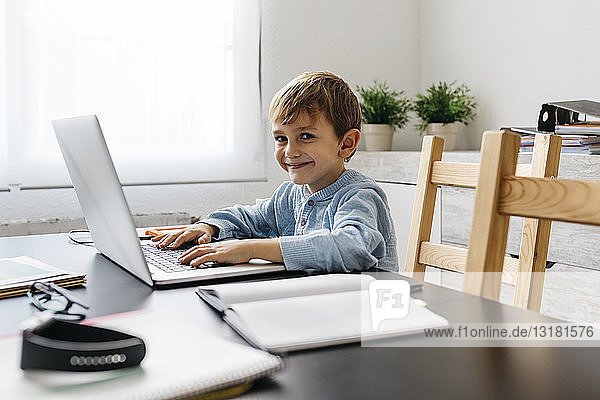 Kleiner Junge sitzt im Büro seines Vaters und benutzt einen Laptop