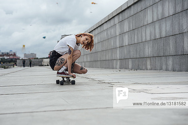 Junge Frau kauert auf einem Carver-Skateboard auf einer Promenade