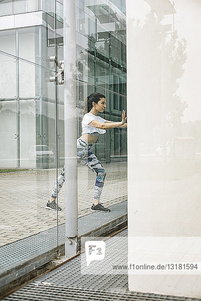 Young woman doing stretching exercise at glass facade