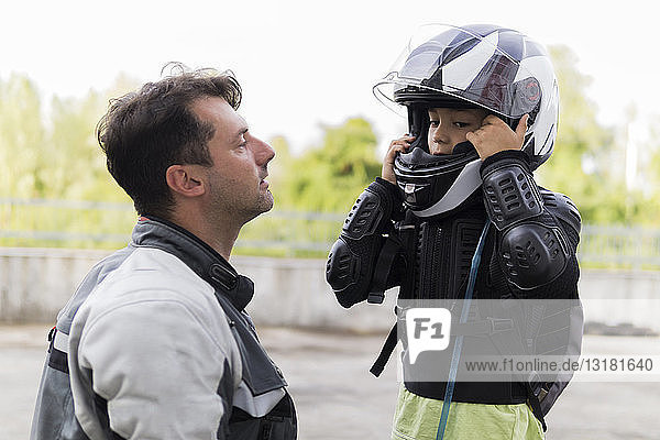 Father watching son putting on motorcycle helmet