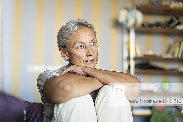 Porträt einer nachdenklichen älteren Frau  die zu Hause auf der Couch sitzt