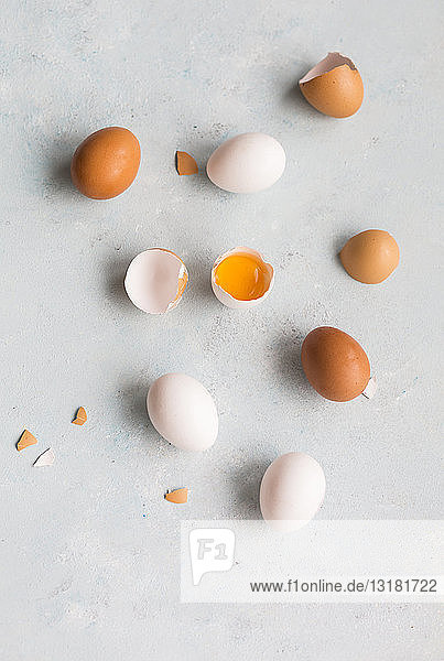 Ganze und geöffnete weiße und braune Eier auf hellem Boden