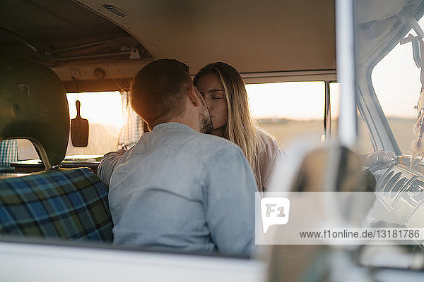 Young couple kissing in camper van at sunset