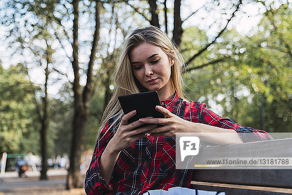 Junge Frau sitzt auf Bank im Freien und benutzt Mini-Tablett