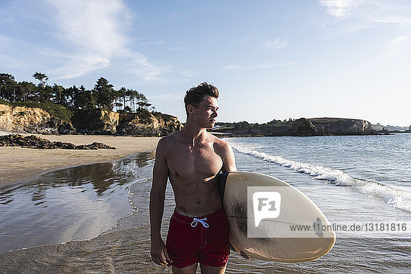 Frankreich  Bretagne  junger Mann mit Surfbrett am Meer stehend