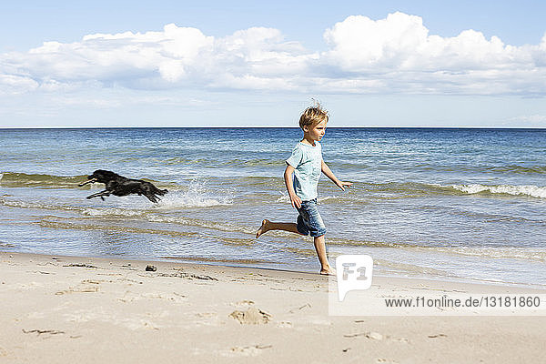 Junge mit Hund rennt am Strand