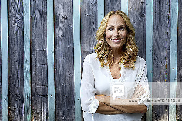 Porträt einer lächelnden blonden Frau vor einer Holzwand