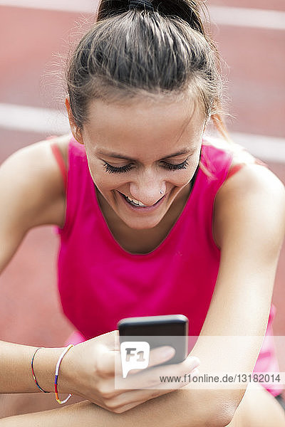 Teenage girl sitting on race track  using smartphone