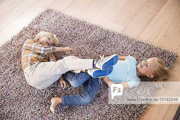 Verspielte Geschwister liegen zu Hause auf Teppich