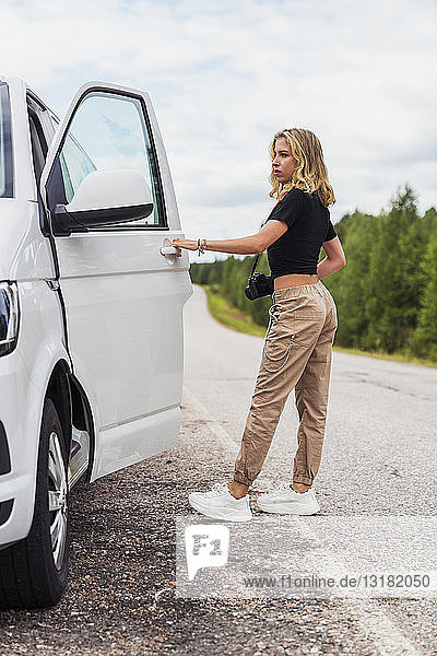 Finnland  Lappland  junge Frau auf der Landstraße beim Einsteigen ins Auto