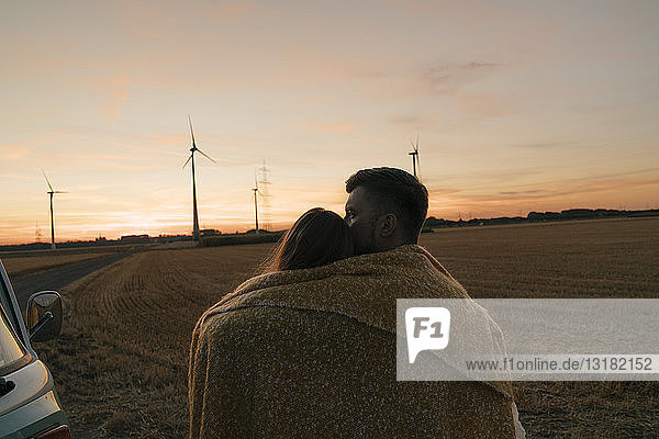 In eine Decke gehülltes Ehepaar im Wohnmobil in ländlicher Landschaft mit Windturbinen im Hintergrund