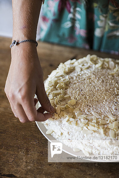 Frauenhand garniert selbstgebackenen Kuchen mit Mandelsplittern  Nahaufnahme