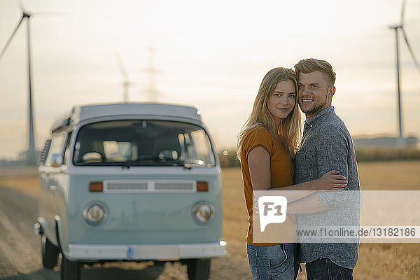 Happy affectionate young couple at camper van in rural landscape