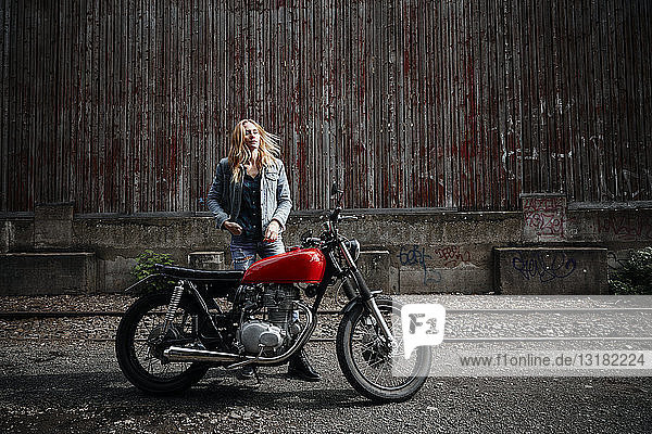 Selbstbewusste junge Frau steht neben dem Motorrad