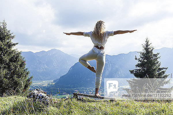 Deutschland  Bayern  Oberammergau  junge Frau macht Yoga auf einer Bank auf einer Bergwiese
