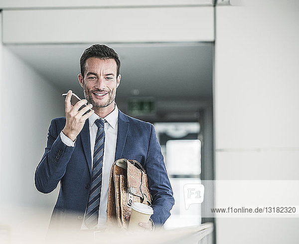 Geschäftsmann mit Aktenkoffer geht mit Smartphone in Bürogebäude