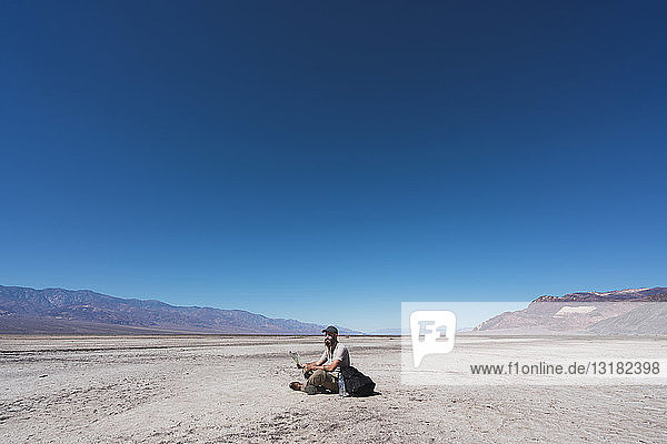 USA  Kalifornien  Death Valley  Mann mit Karte sitzt auf dem Boden in der Wüste und ruht sich aus