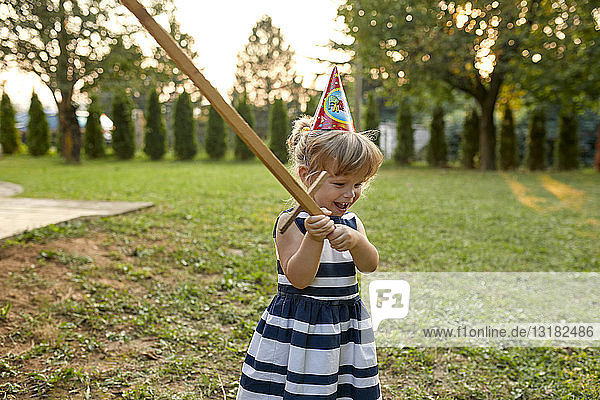 Glückliches kleines Mädchen mit Partyhut und Holzschwert im Garten