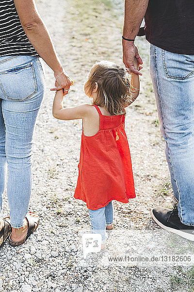 Mädchen geht auf den Händen der Eltern auf einem Feldweg