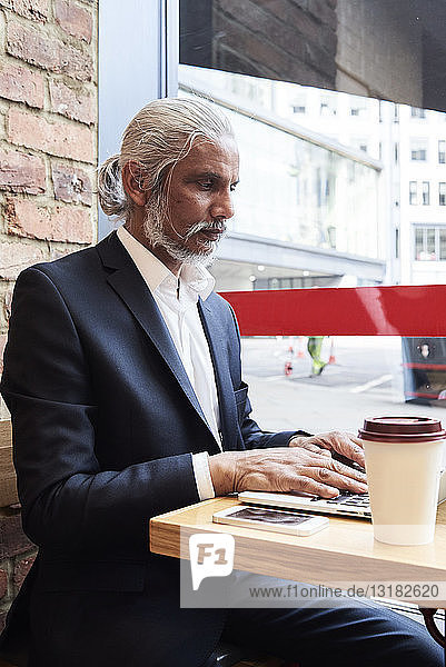 Leitender Geschäftsmann sitzt in einem Café und arbeitet am Laptop