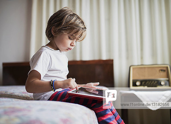 Young boy sitting on bed using a tablet