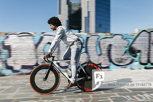 Mittelgroßer erwachsener Mann fährt Fahrrad vor einer Graffiti-Wand