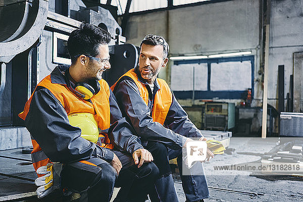 Two men wearing protective workwear talking during break in factory