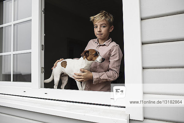 Portrait of boy with Jack Russel Terrier looking out of open window