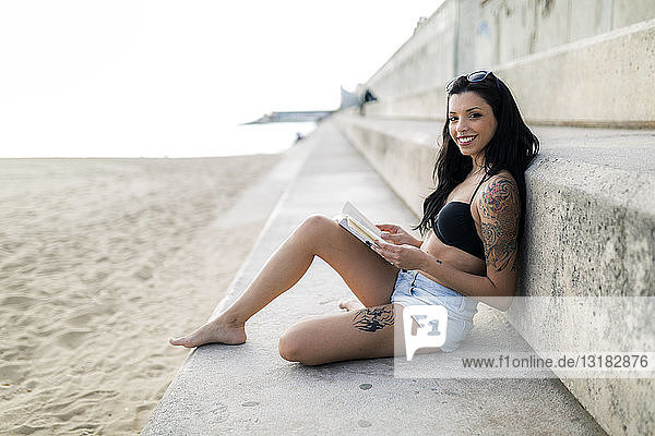Portrait of tattooed young woman reading a book near the beach