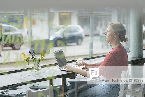 Junge Frau mit Tasse Kaffee und Laptop am Fenster in einem Café