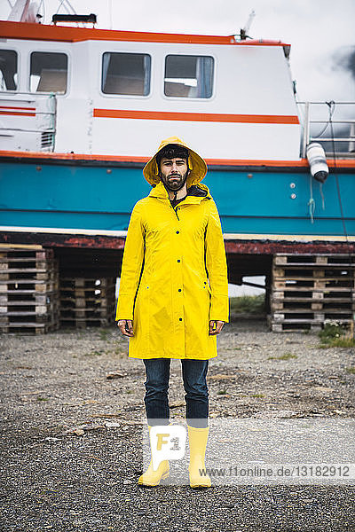 Junger Mann steht vor einem Schiff und trägt Regenkleidung  Lappland  Norwegen