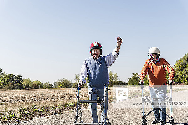 Two old friends wearing safety helmets  competing in a wheeled walker race
