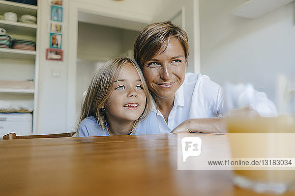 Lächelnde Mutter und Tochter sitzen zu Hause am Küchentisch