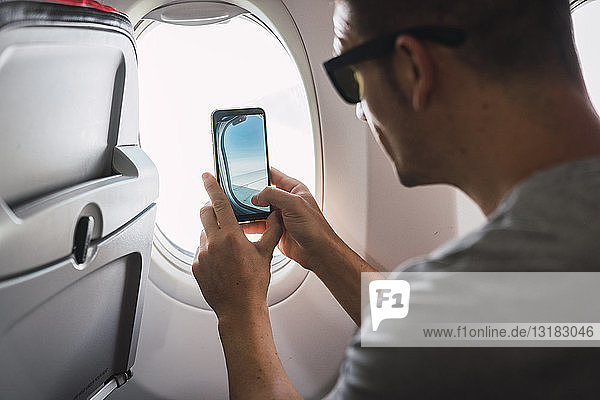 Man in airplane  using smartphone  taking a picture  airplane window