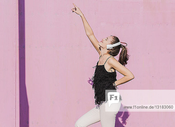 Glückliche junge Frau mit Kopfhörern tanzt vor rosa Wand