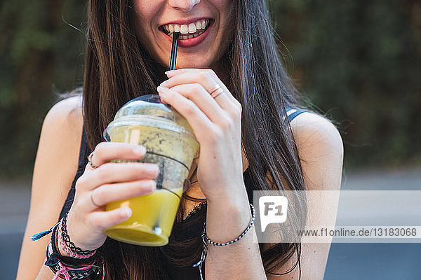 Lächelnde Frau trinkt Saft mit einem Strohhalm