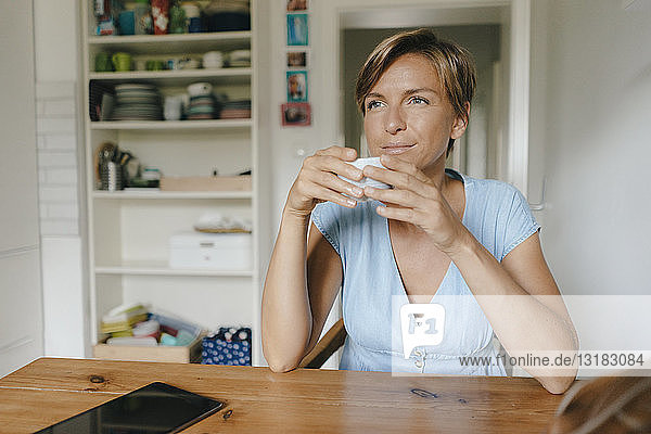 Frau sitzt zu Hause am Tisch mit einer Tasse Kaffee