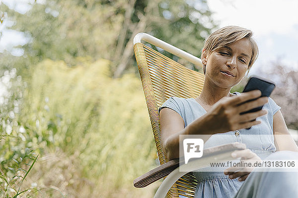 Woman sitting in garden on chair using cell phone