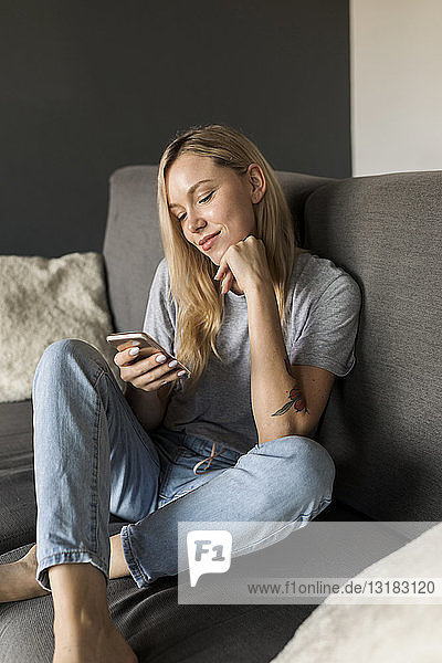 Smiling young woman sitting on couch using cell phone