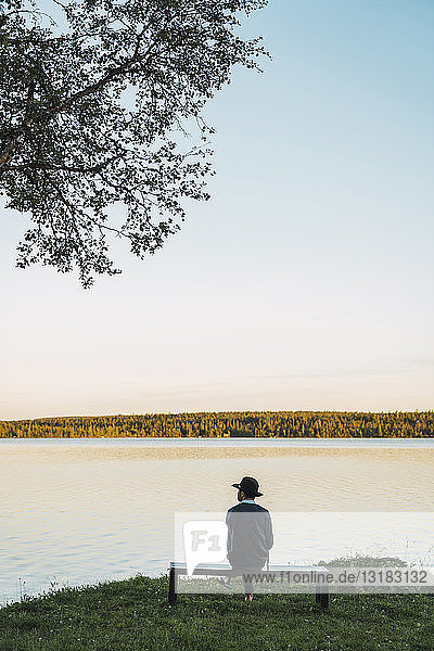 Junger Mann sitzt auf einer Bank und schaut auf den See