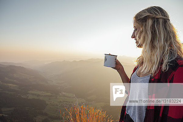 Schweiz  Grosse Mythen  junge Frau auf einer Wanderung bei Sonnenaufgang mit einem Becher in der Hand