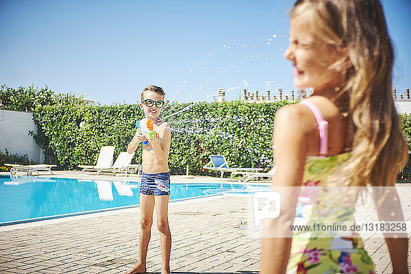 Junge mit Wasserpistole spritzt auf Mädchen am Pool