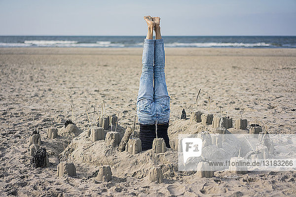 Eine reife Frau macht einen Kopfstand am Strand in einer Sandburg